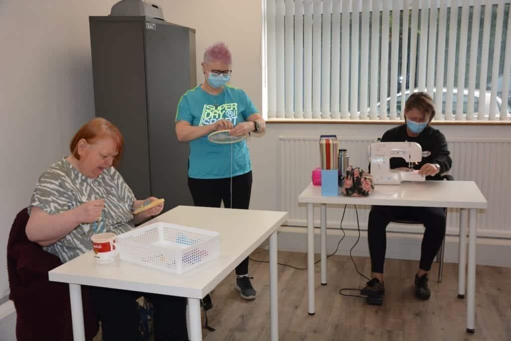 Weaving Magic at Prospect House 3 a Pure client embroiders a bird on cloth and a staff member works at a sewing machine.