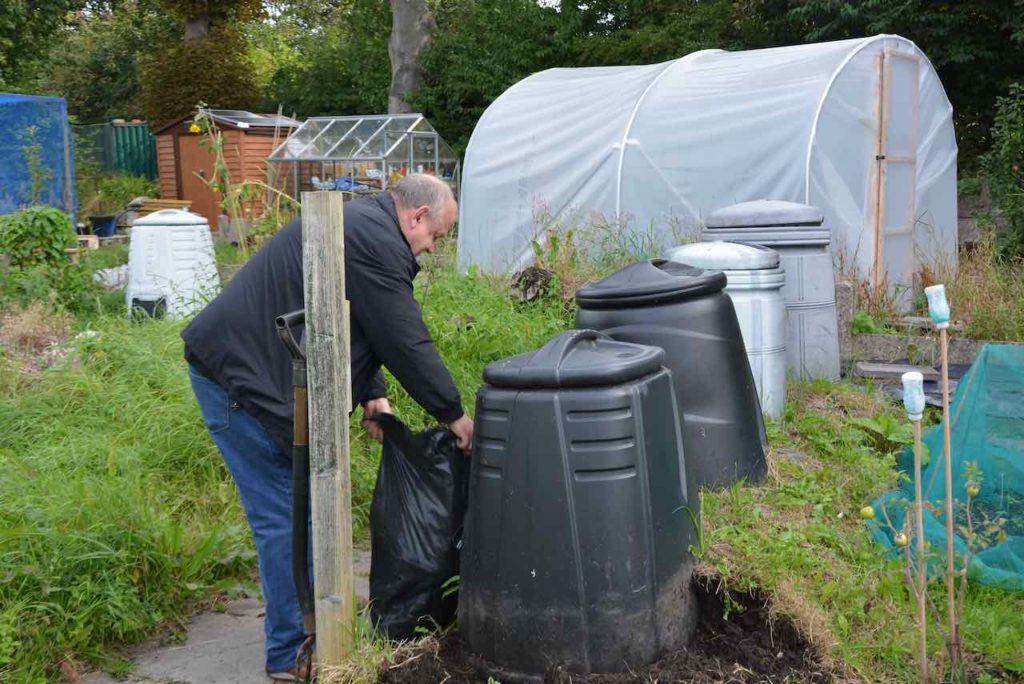 A man moves bagged garden waste to the black compost bins
