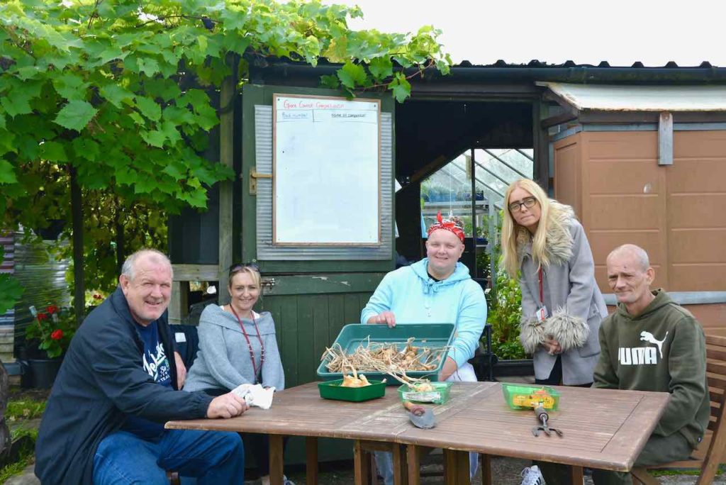 MHN clients sit by a table with the onion harvest alogn with satff members Lisa and Lucy
