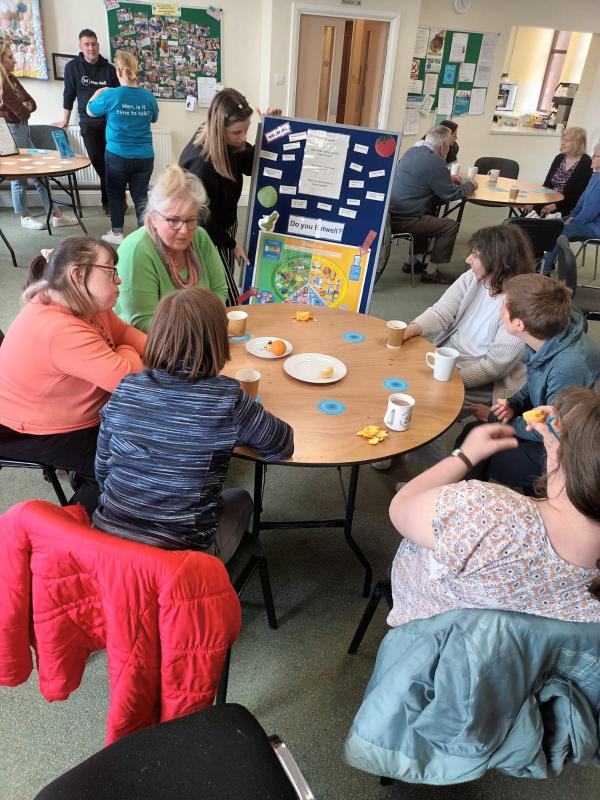 The Community Hub 13 People sat round wooden table with coats on back of chairs
